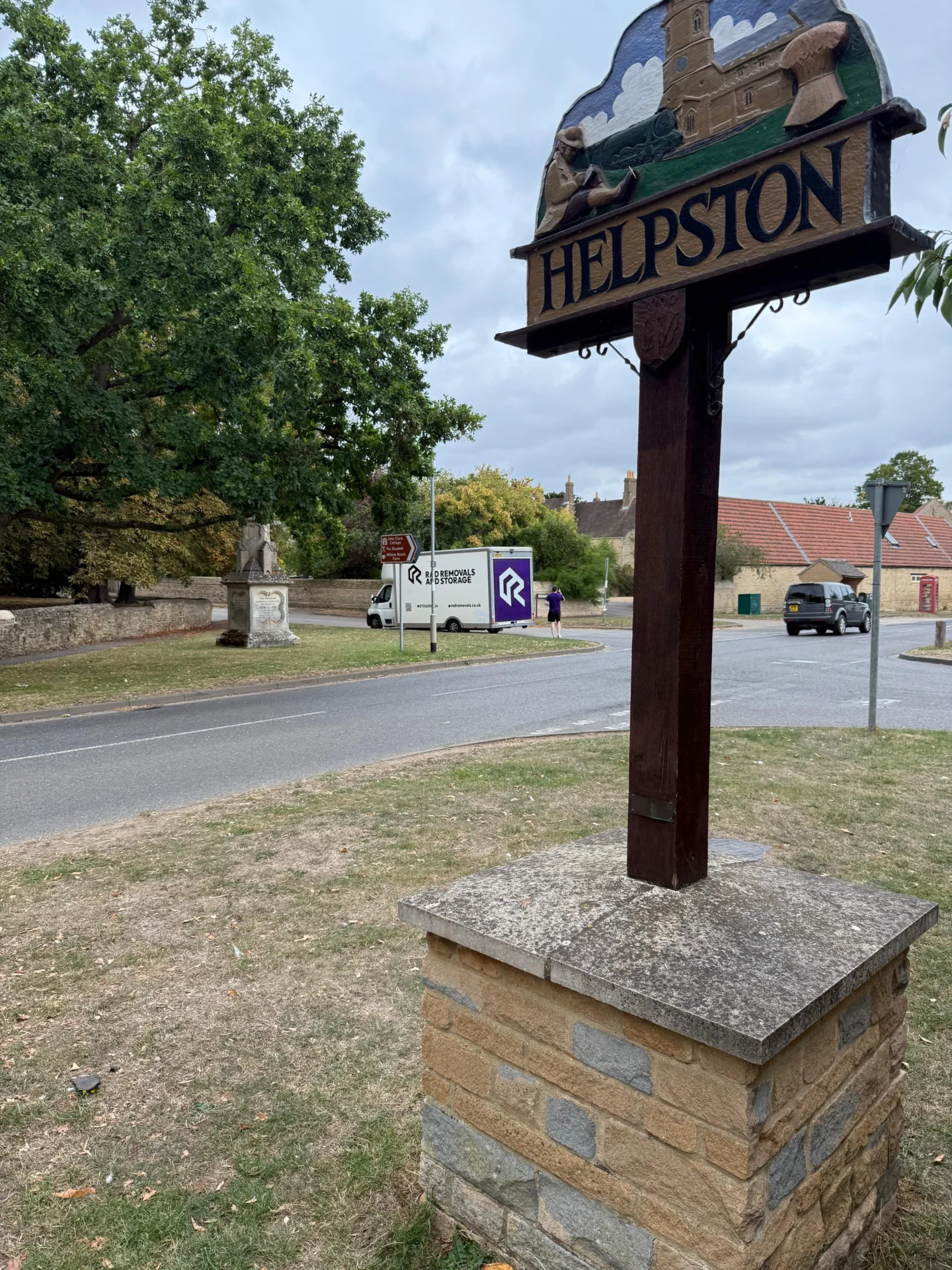 Rad Removals van driving into Helpston with town sign in foreground and open countryside behind